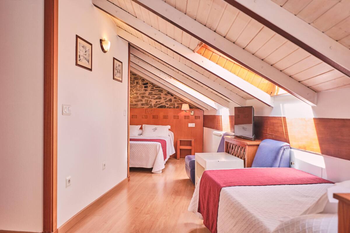 Une chambre confortable située dans les combles, avec des poutres en bois, un mur en pierre et un lit recouvert d’une couverture rouge.
