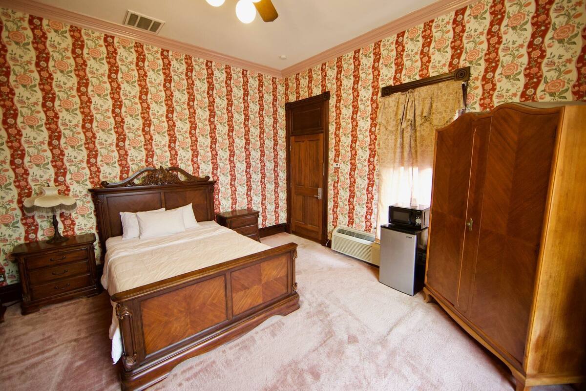 A bedroom with a wooden bed, a wardrobe, a nightstand, a lamp, and a heater.