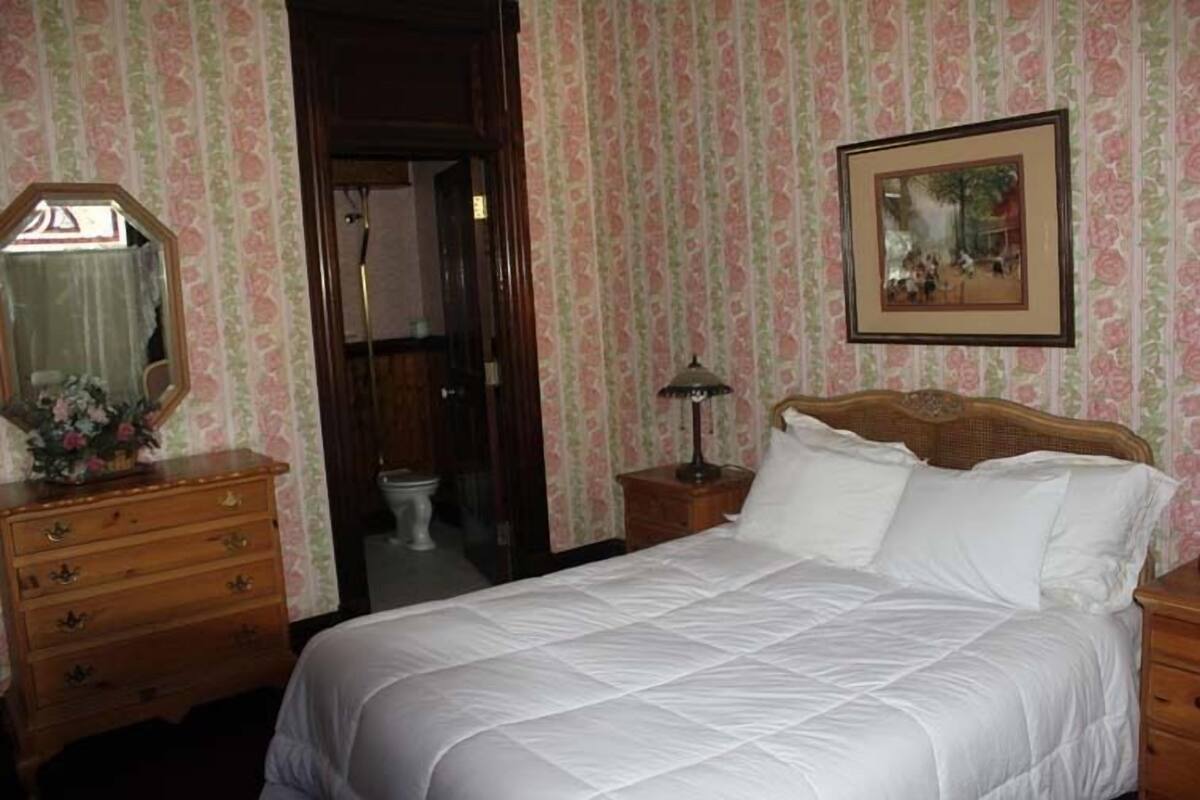A bedroom with a bed, wooden dresser, and a framed picture on the wall.
