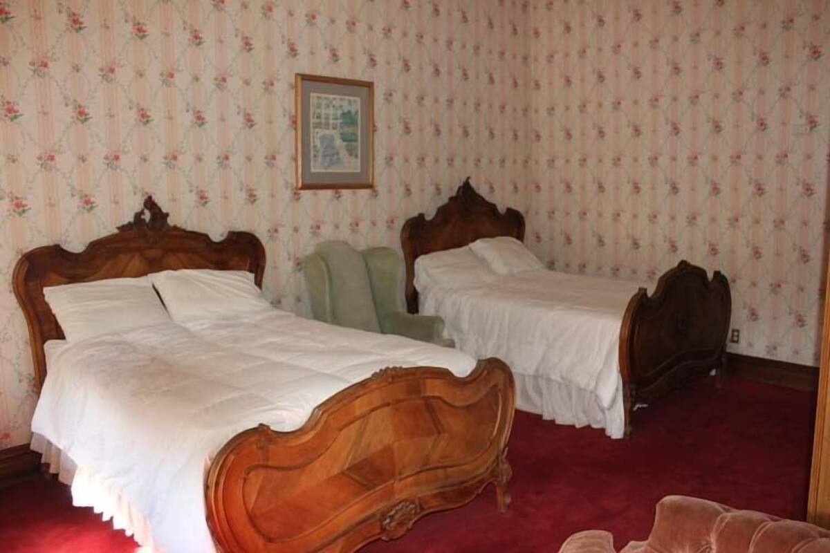 A bedroom with two wooden beds, a green chair, and floral wallpaper.