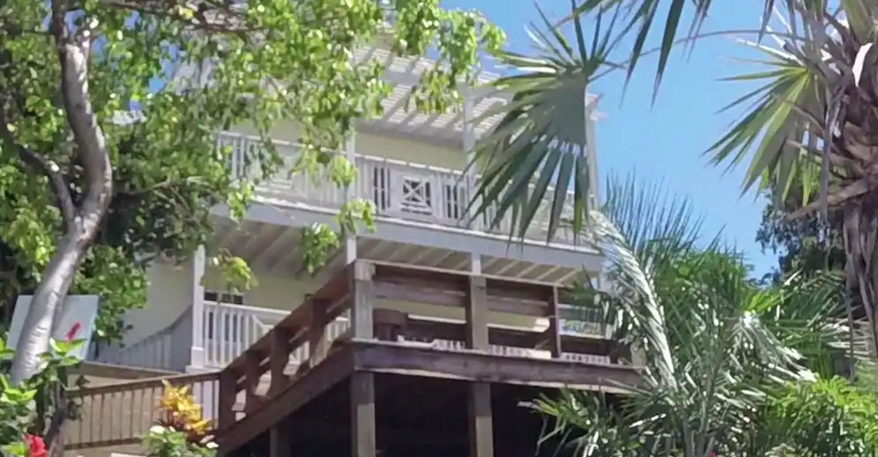 Ein zweistöckiges Gebäude mit Balkon und überdachtem Bereich, umgeben von üppiger Vegetation.