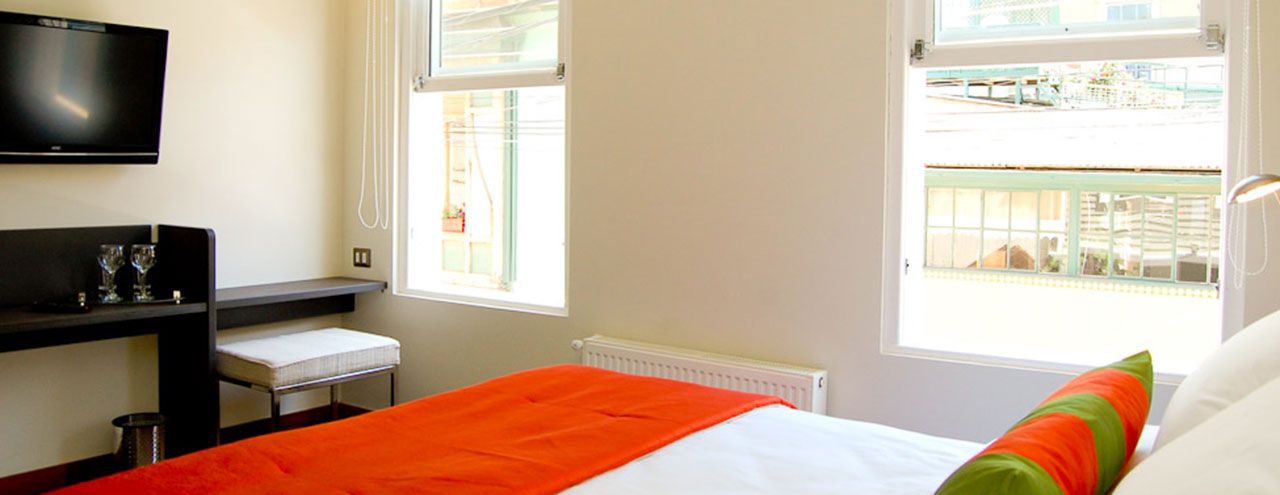 Una habitación de hotel con cama, televisión montada en la pared, ventana y una mesita con una silla.