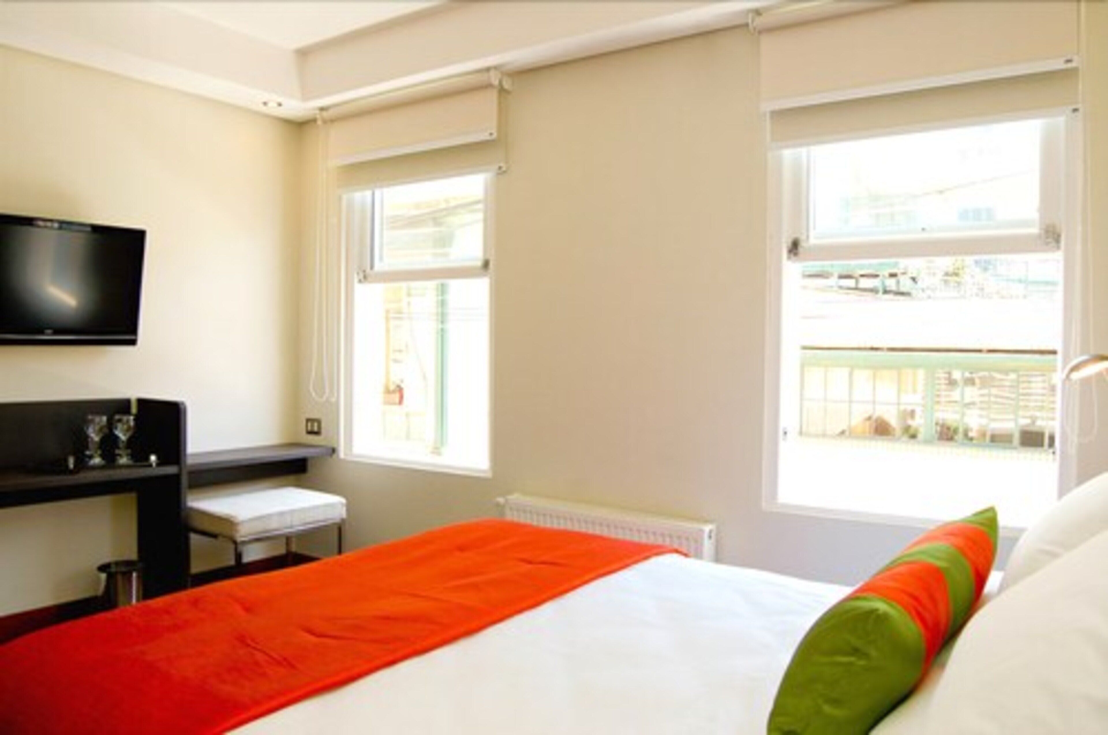 A hotel room with a bed, a TV mounted on the wall, a desk with a chair, and a window with a view of the outside.