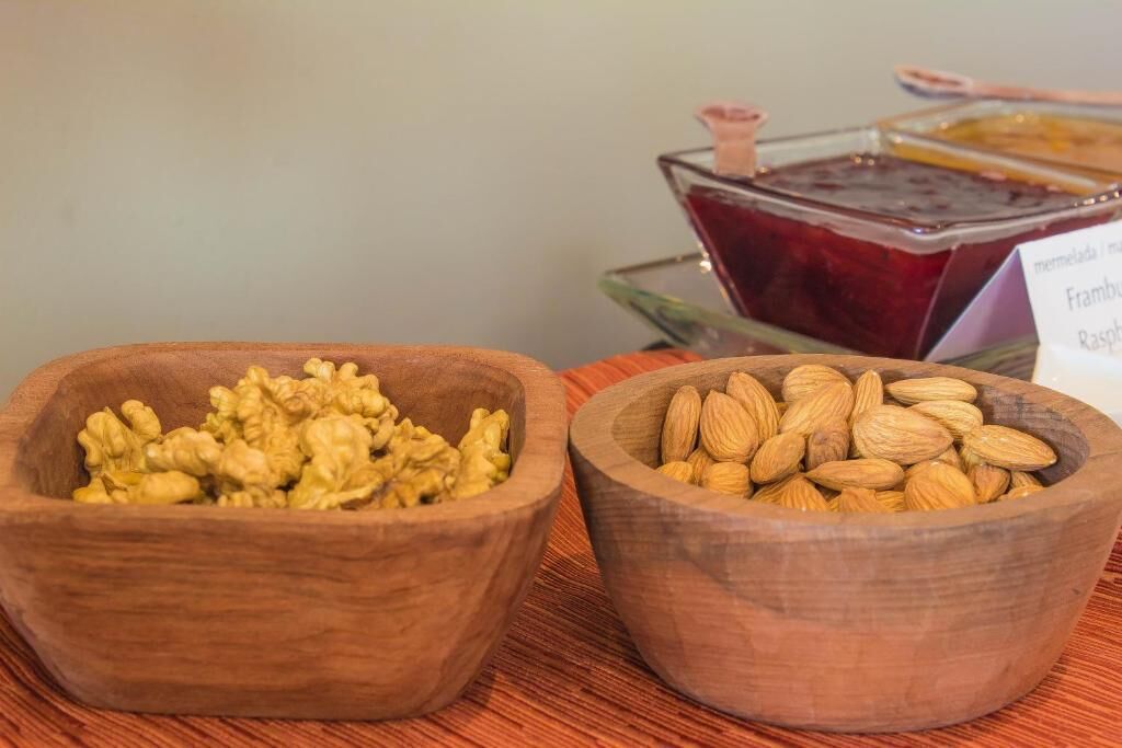 Two wooden bowls filled with walnuts and almonds, placed on a wooden surface with a sign indicating available jams and jellies in the background.