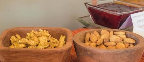 Two wooden bowls filled with walnuts and almonds, placed on a wooden surface with a sign indicating available jams and jellies in the background.