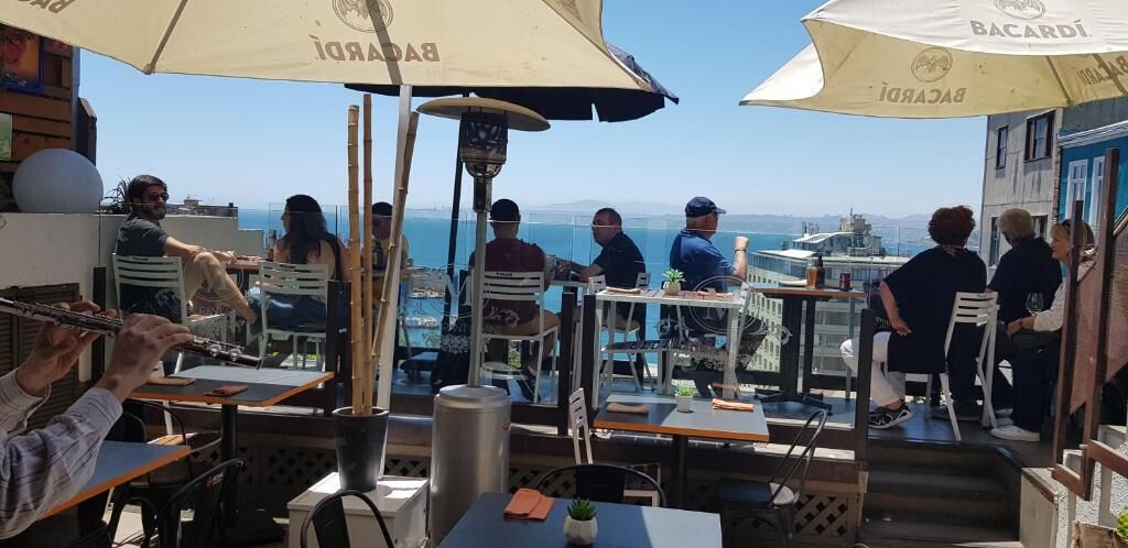 An outdoor dining area with tables and chairs, umbrellas, and a view of the sea.