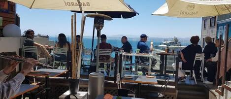 An outdoor dining area with tables and chairs, umbrellas, and a view of the sea.