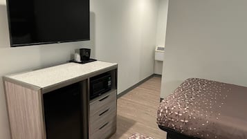 Una habitación de hotel moderna con un televisor de pantalla plana montado en la pared, un microondas y una cafetera pequeña sobre la encimera. Cuenta con una cama con colcha estampada y suelo de madera.