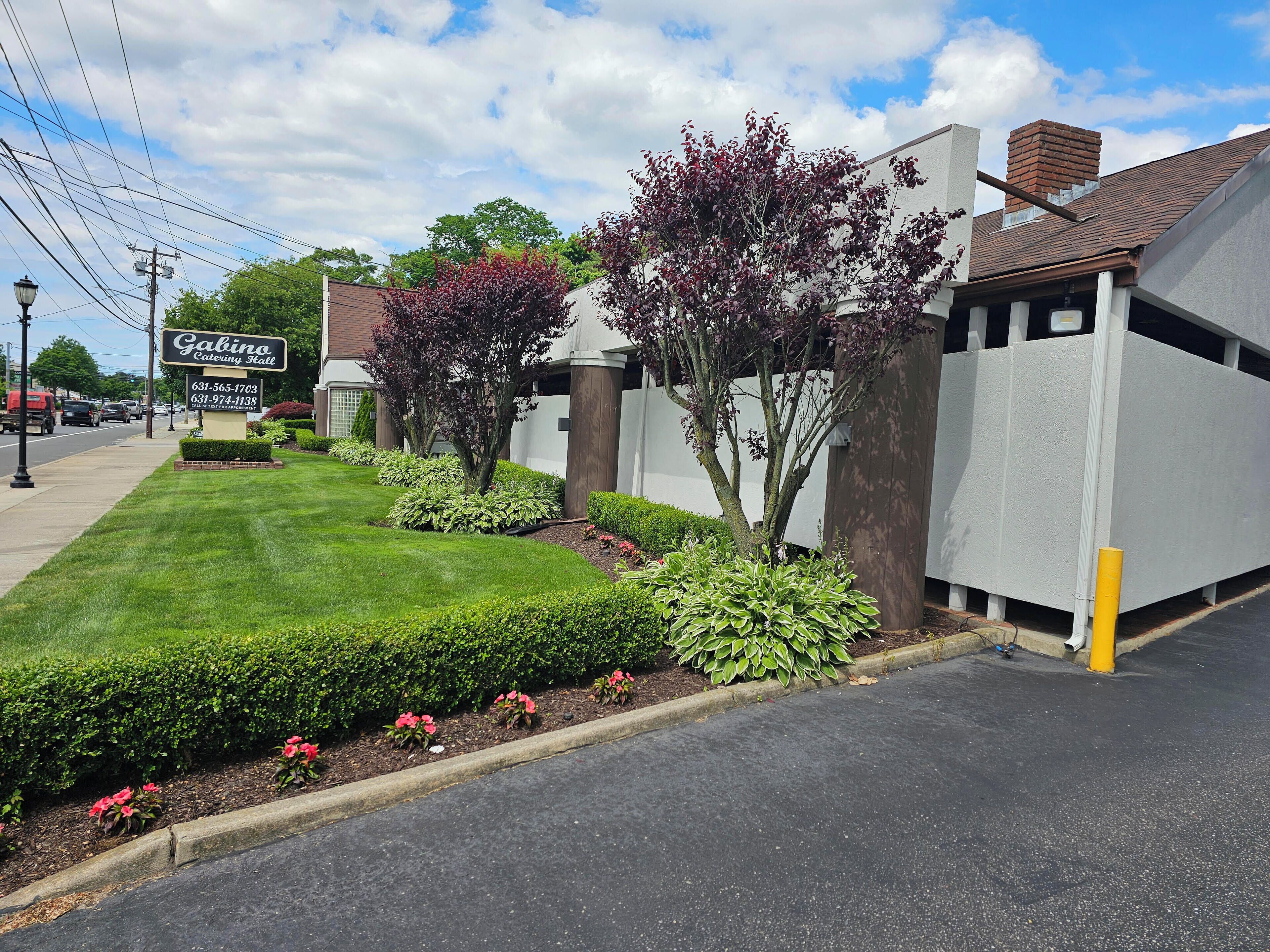 A well-maintained lawn, a sign for 'Gabino Catering Hall', and a building with a brick chimney.