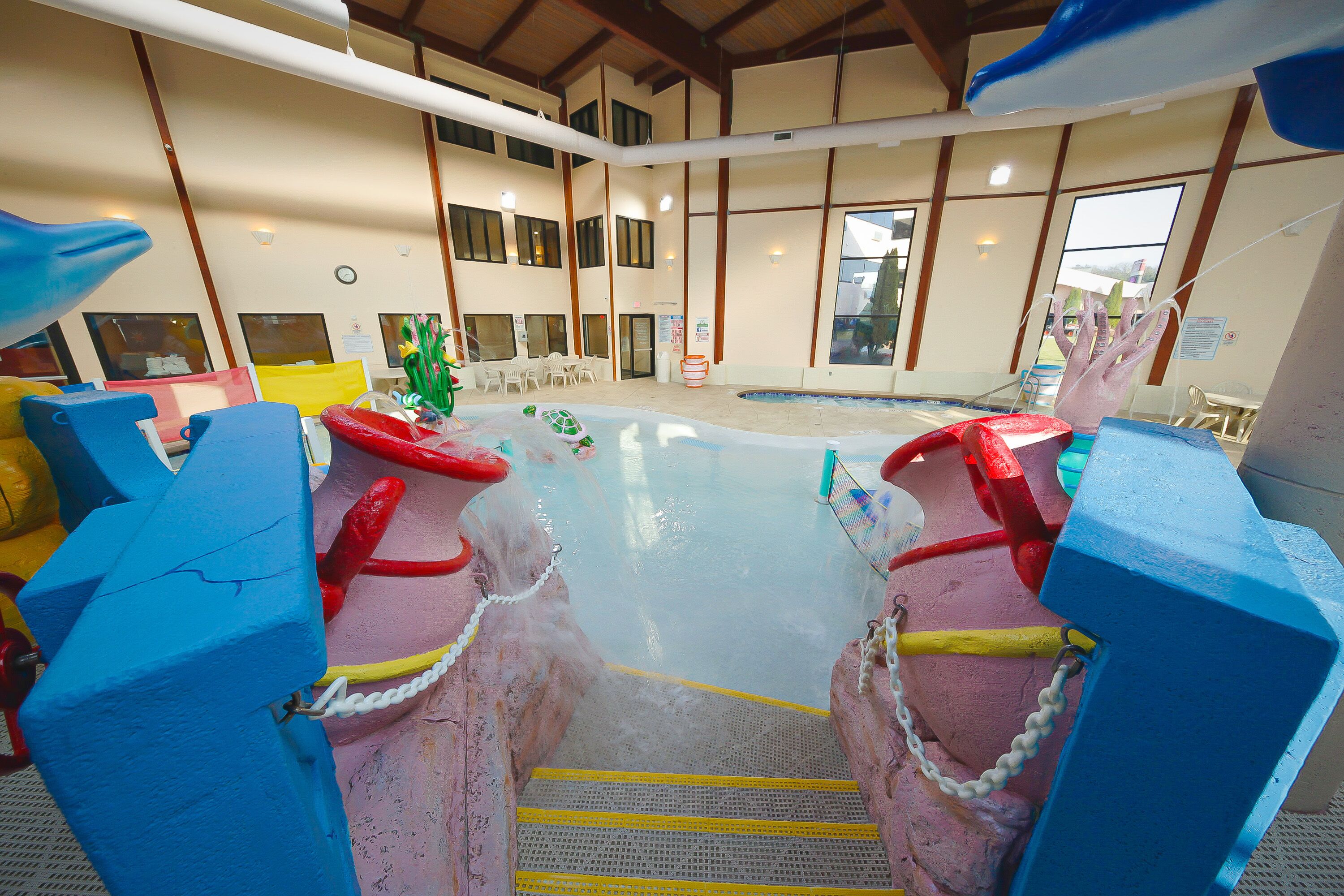 An indoor swimming pool with colorful play structures and steps leading into the water.
