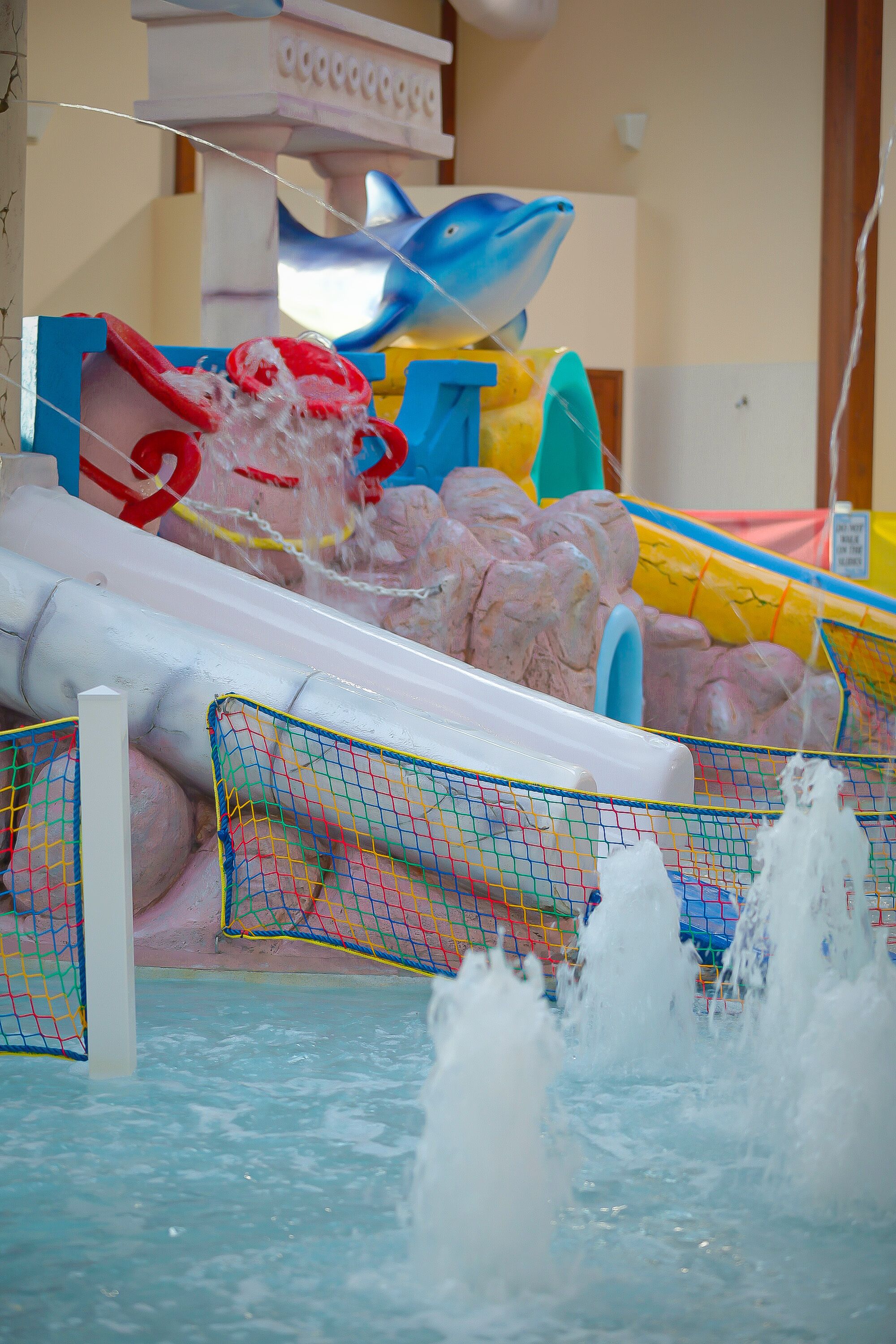 Un espace de jeux aquatiques comprenant un toboggan, des jets d’eau et une structure en forme de dauphin.