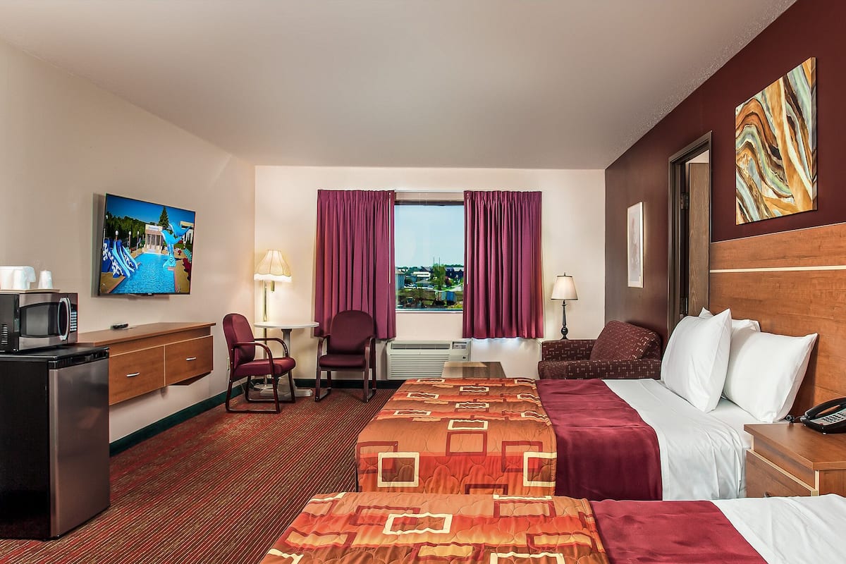 Habitación de hotel con cama, escritorio con computadora, silla, televisor y ventana con cortinas.