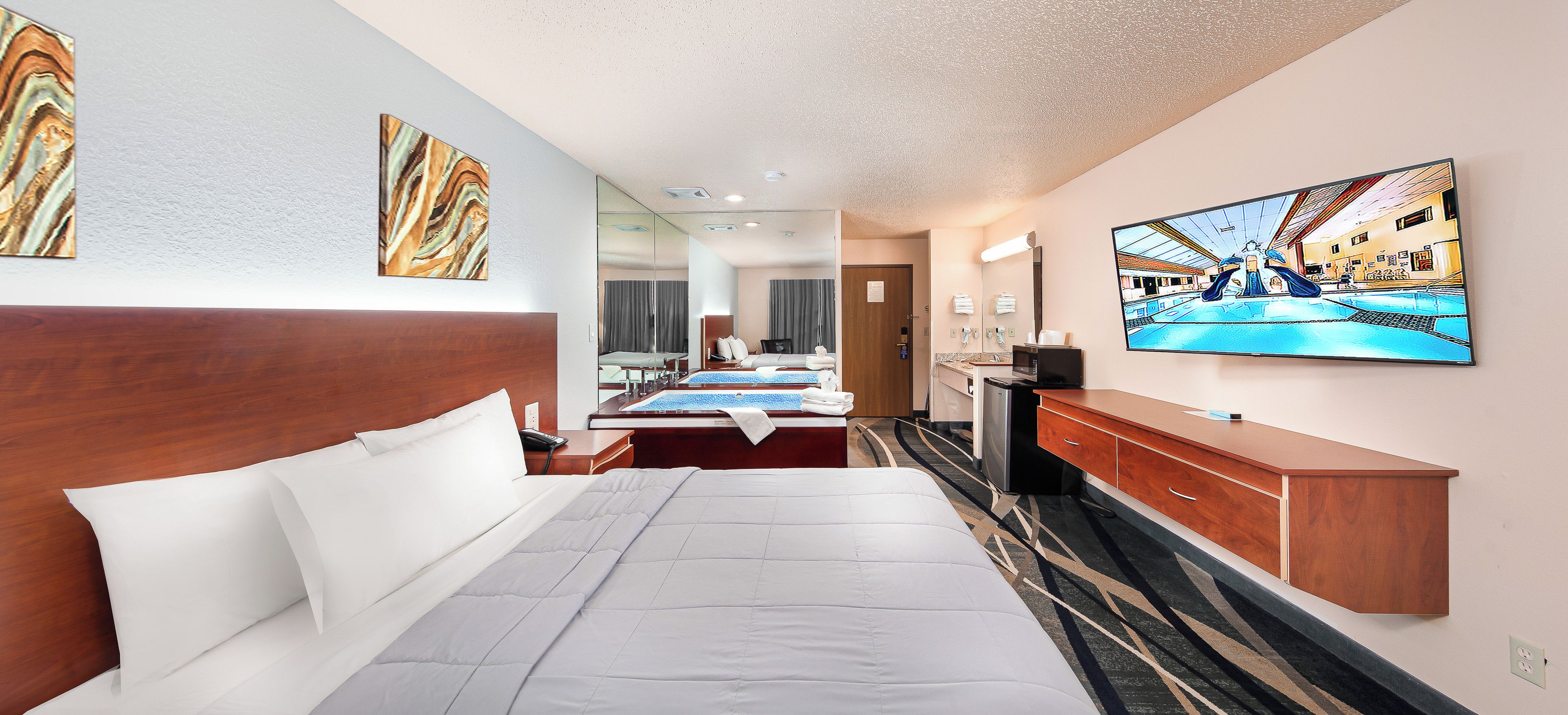 A hotel room with a large bed, a desk, a television, and artwork on the walls.
