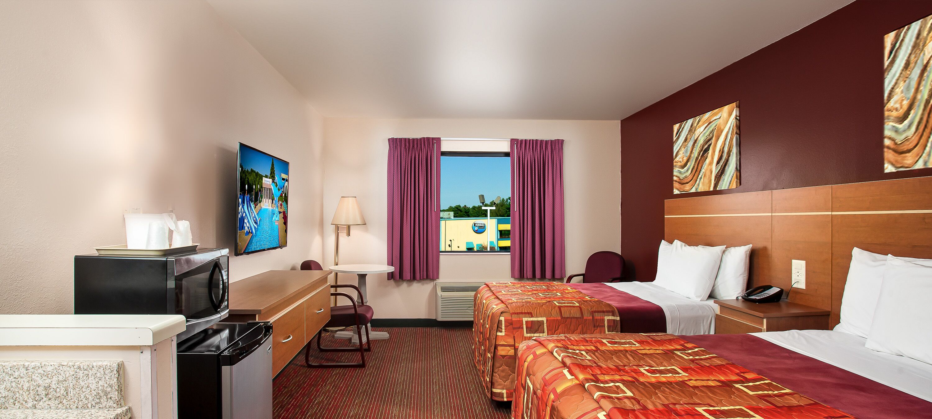 A hotel room with a bed, a desk with a TV, a chair, a table, and a window with curtains.