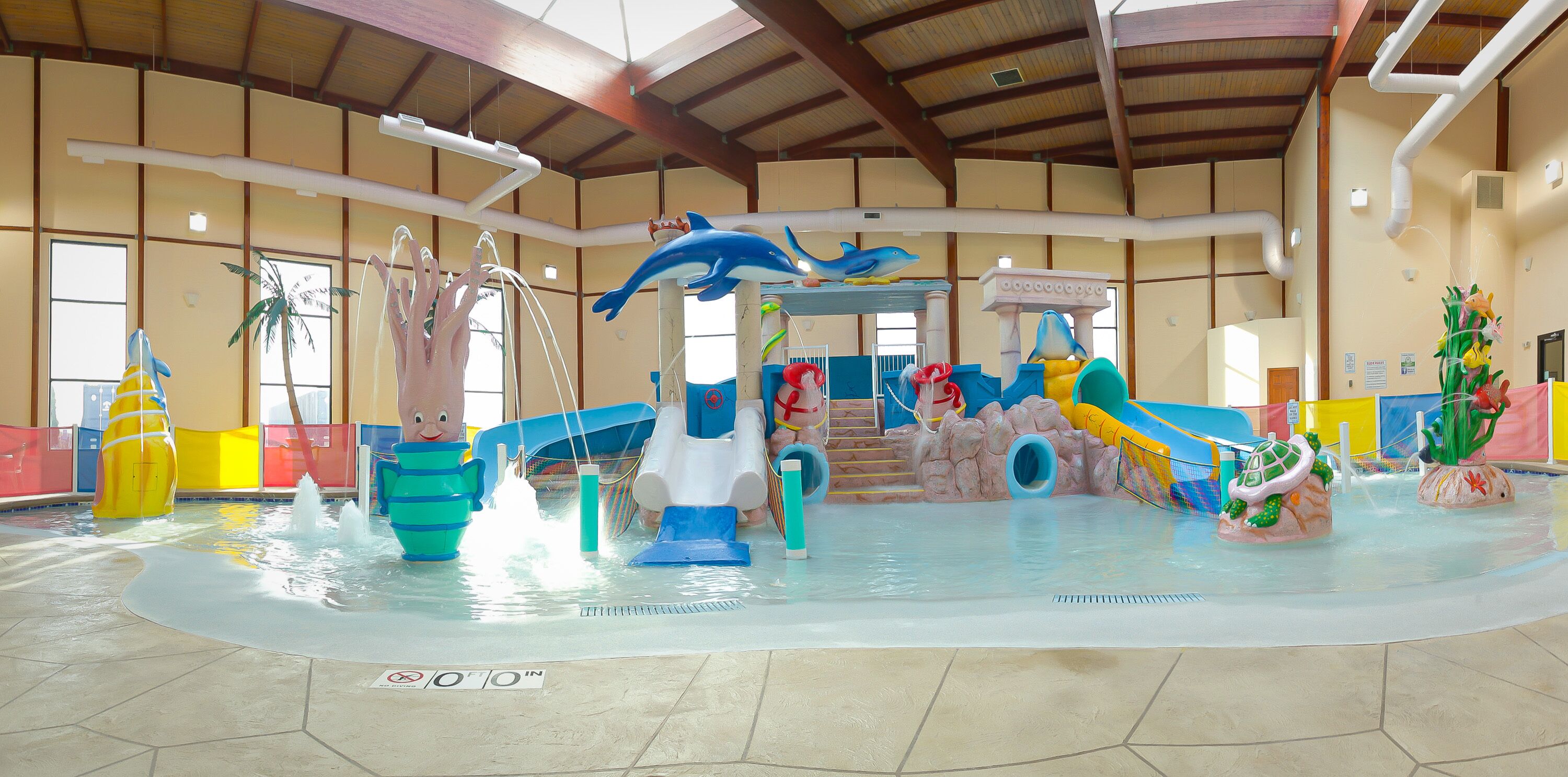 An indoor water park with various water play structures, including slides and splash pads.