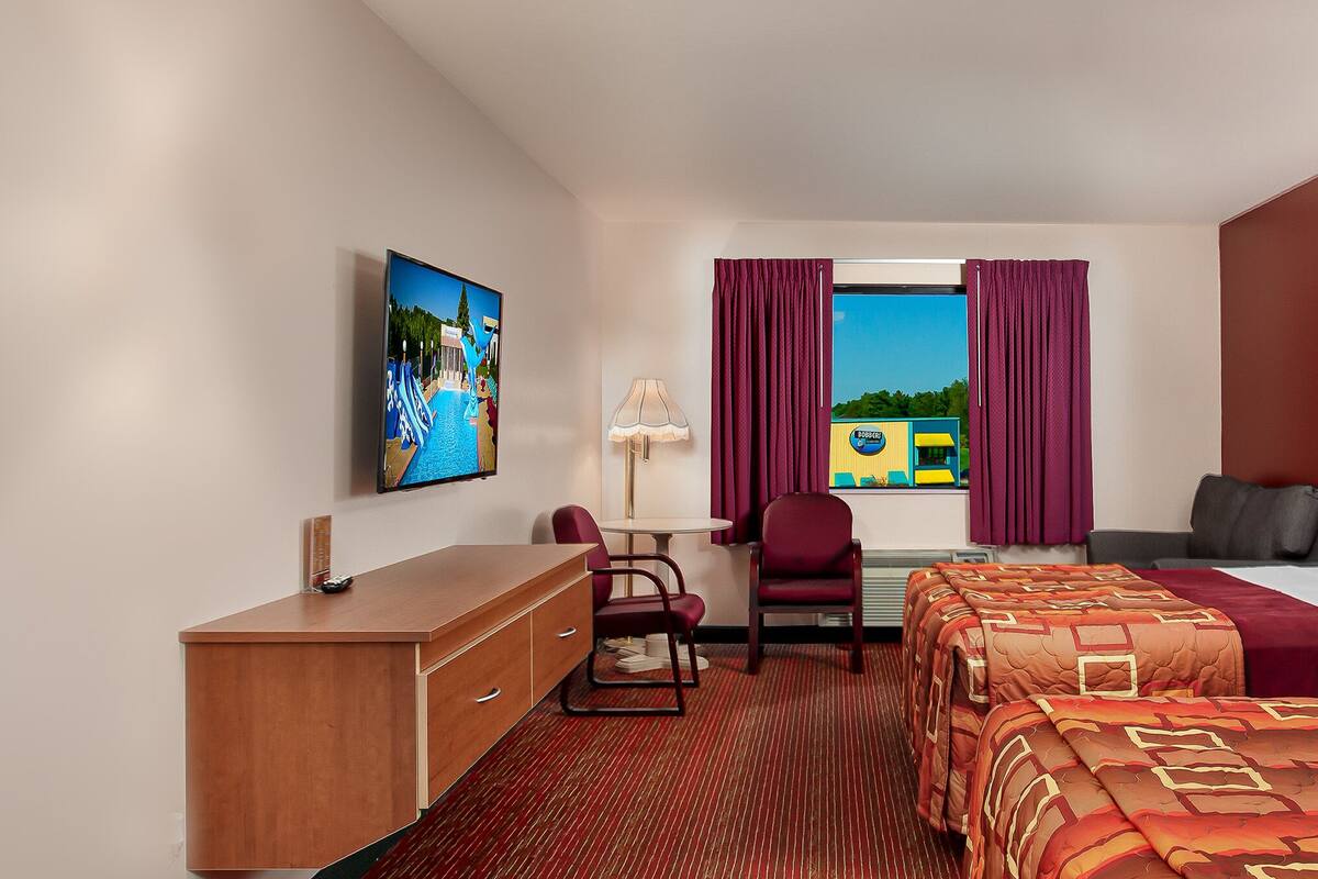 Habitación de hotel con dos camas, un escritorio, una silla, una lámpara y obras de arte en las paredes.