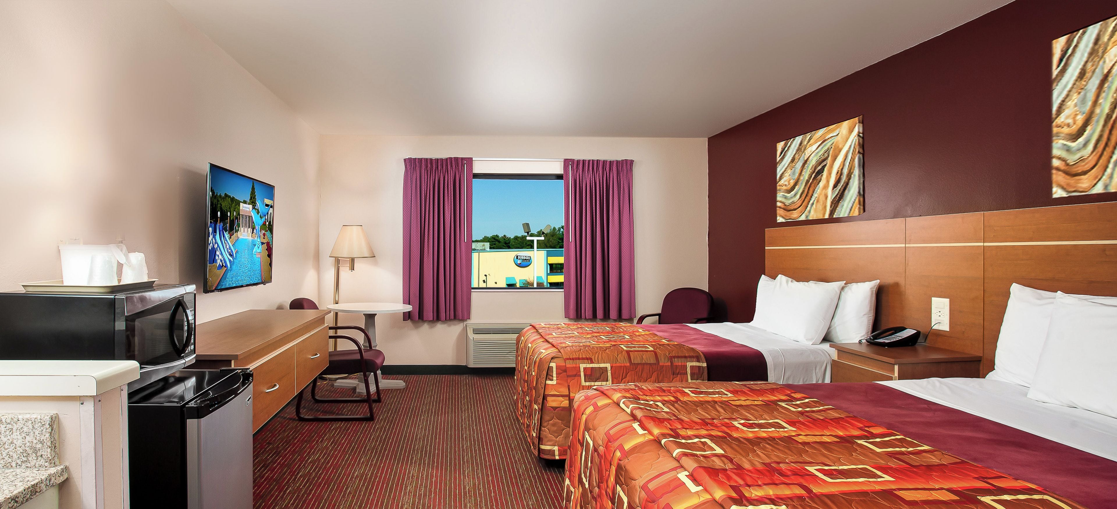 Een hotelkamer met een bed, een bureau met een computer, een stoel, een televisie en een raam met gordijnen.