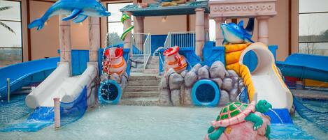 An indoor water play area with slides, a dolphin statue, and a turtle statue.