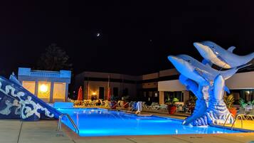 A swimming pool with a dolphin sculpture, lounge chairs, and a building in the background.