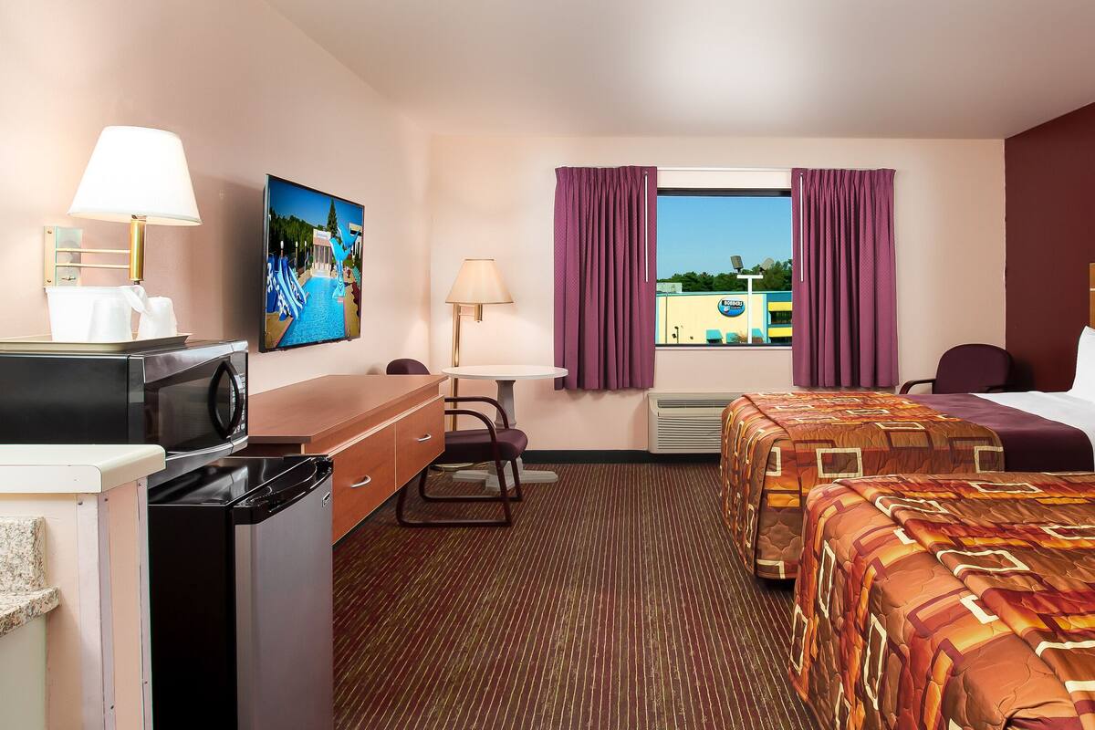 Una habitación de hotel con cama, escritorio, silla, televisor y ventana con cortinas.