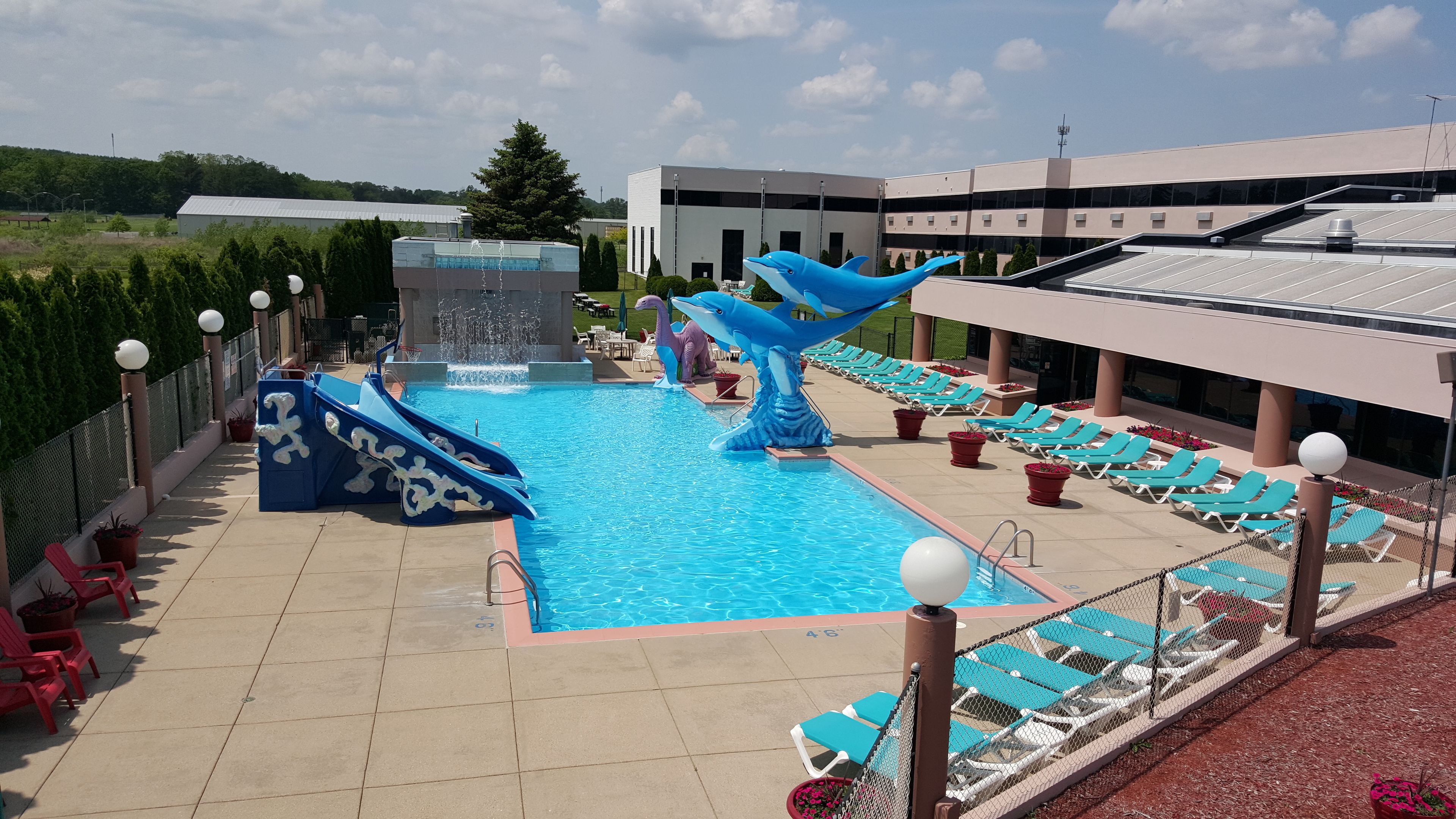 A swimming pool with slides and a dolphin sculpture, surrounded by lounge chairs and potted plants.