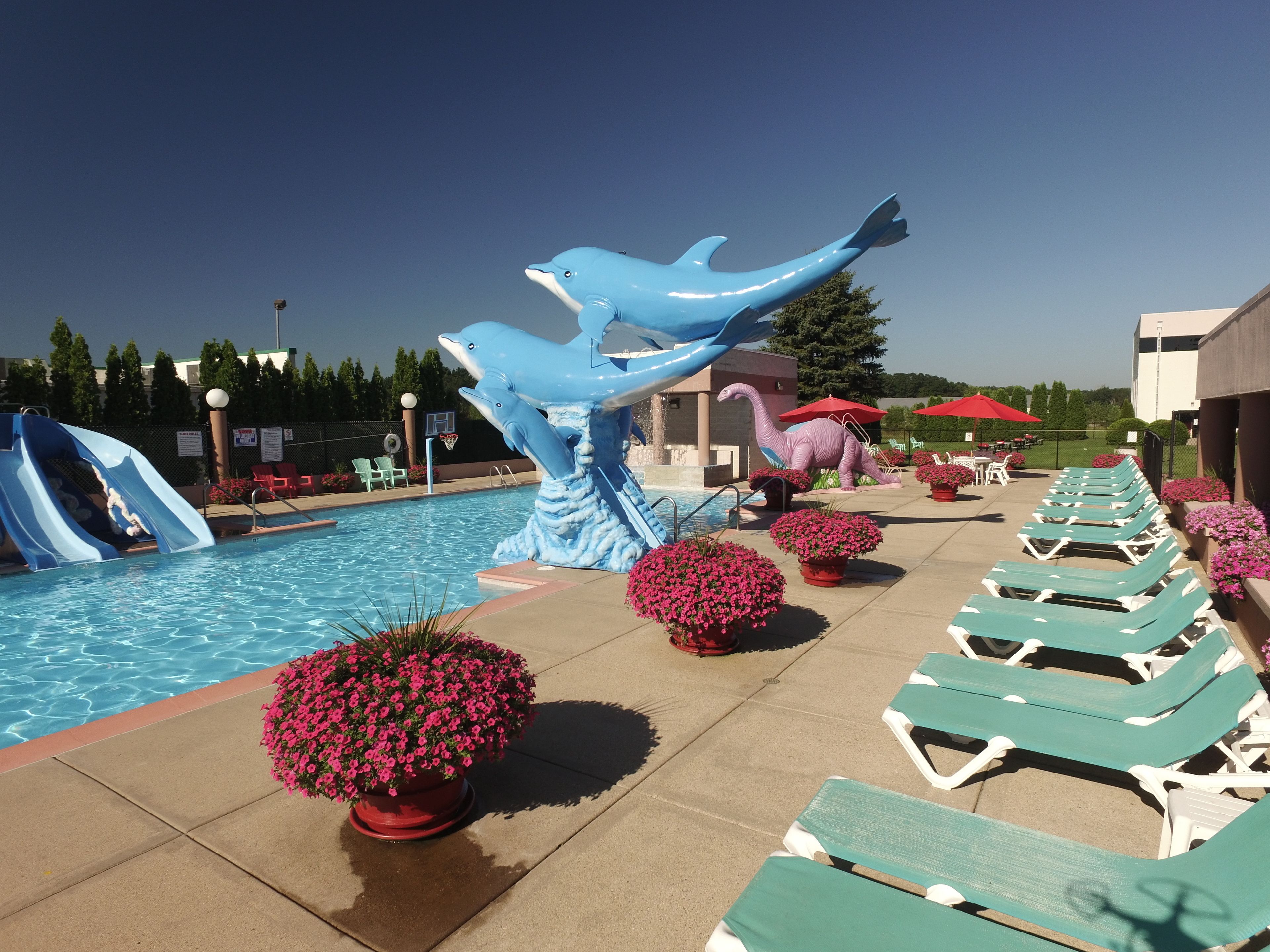 A swimming pool with a dolphin sculpture, lounge chairs, and potted plants.