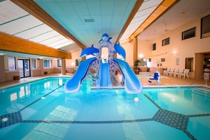 An indoor swimming pool with a dolphin slide and a seating area with chairs.