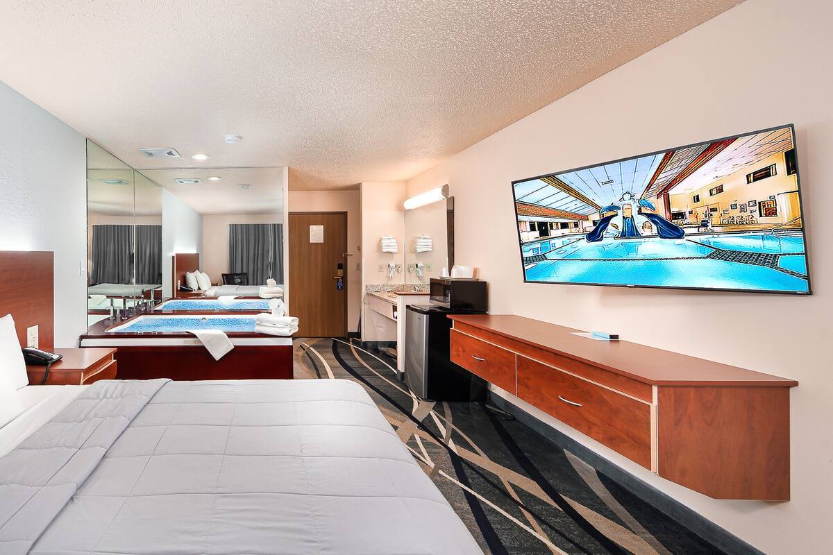 Habitación de hotel con una cama grande, televisión, escritorio y baño visible a través de un mamparo de vidrio.