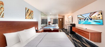 A hotel room with a large bed, a TV, a desk, and a bathroom visible through a glass partition.
