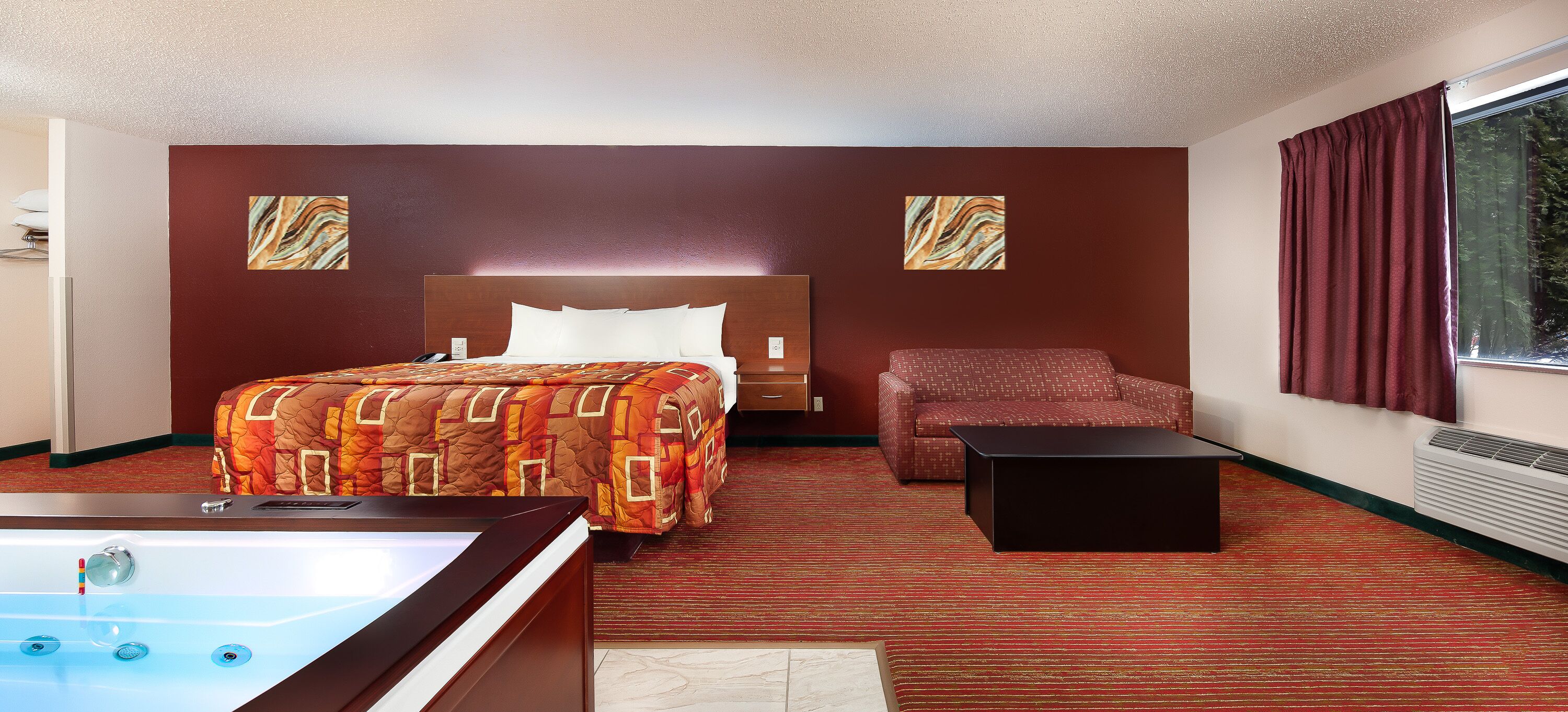 A hotel room with a bed, a sofa, a small table, a bathtub, and a window with curtains.