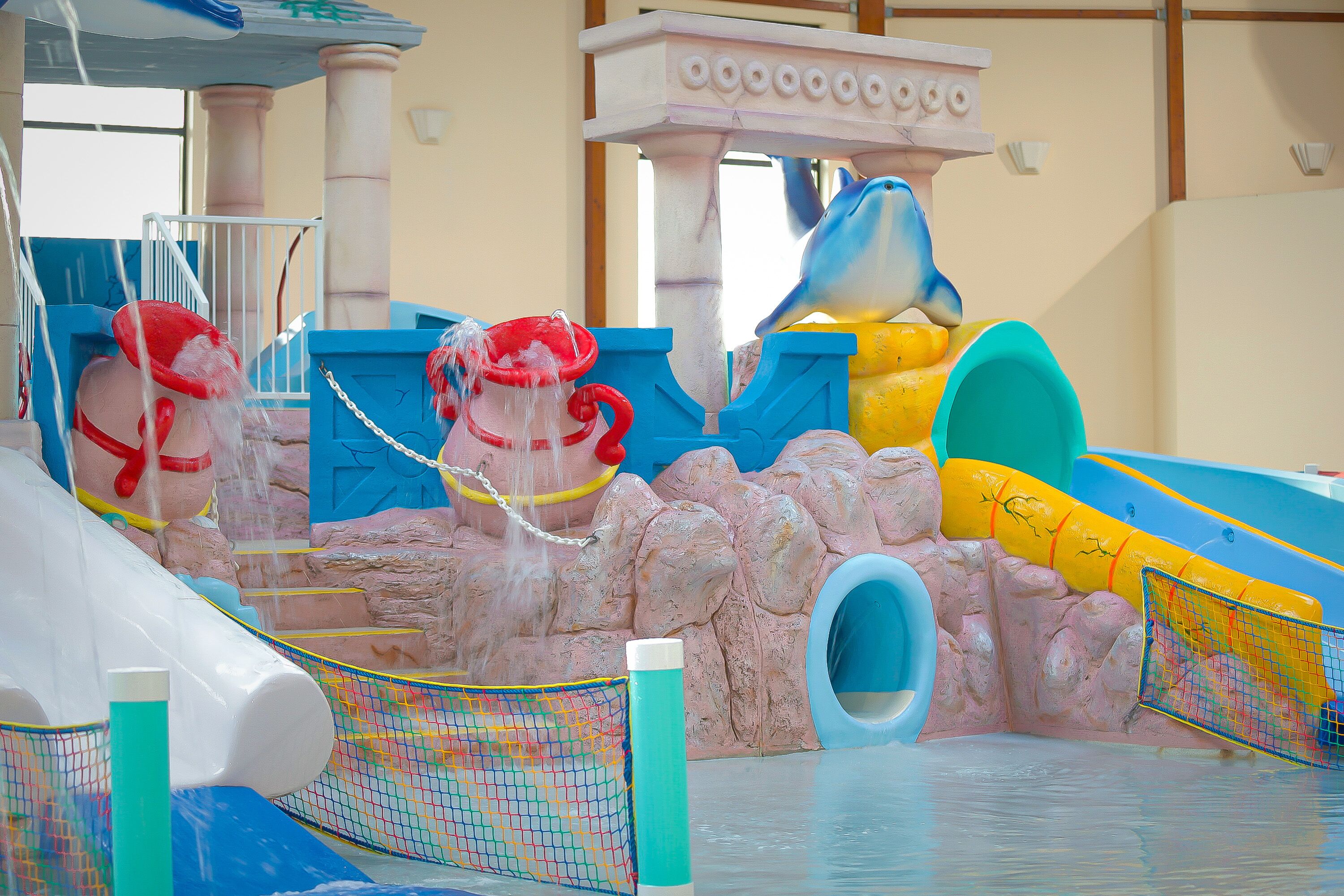 A water play area with slides, a rock wall, and a dolphin statue.