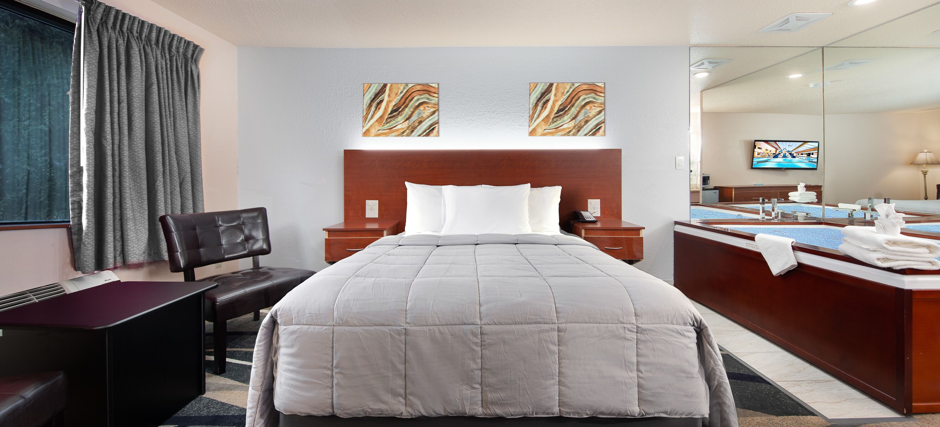 A hotel room with a large bed, a desk, a chair, a desk lamp, a telephone, a mirror, and artwork on the wall.