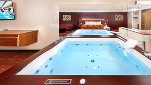Une chambre d’hôtel dotée d’un grand espace spa, d’un lit, d’une télévision et d’une salle de bain avec un miroir et un porte-serviettes.