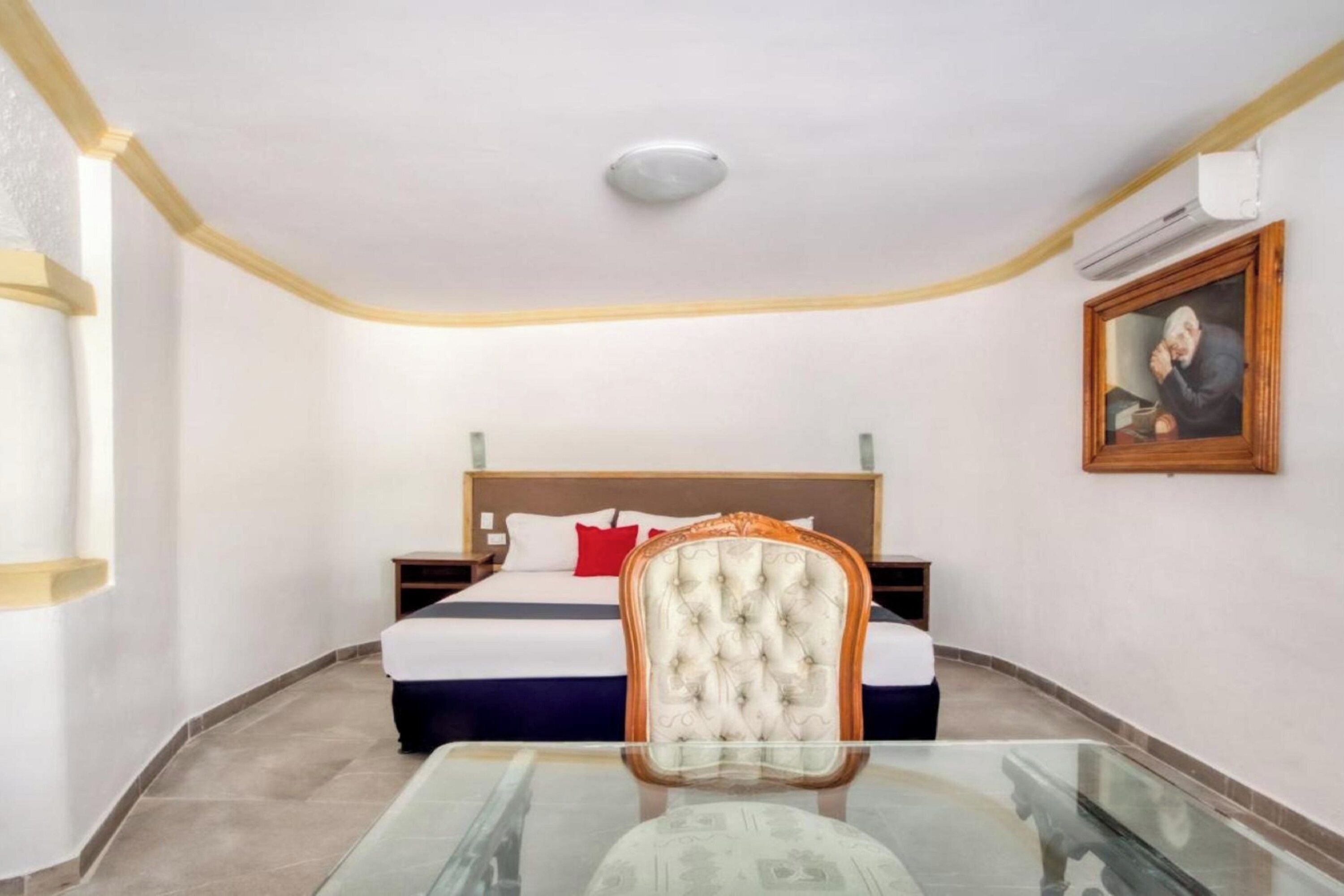 Une chambre d’hôtel avec un lit, une table en verre, une chaise et un tableau au mur.