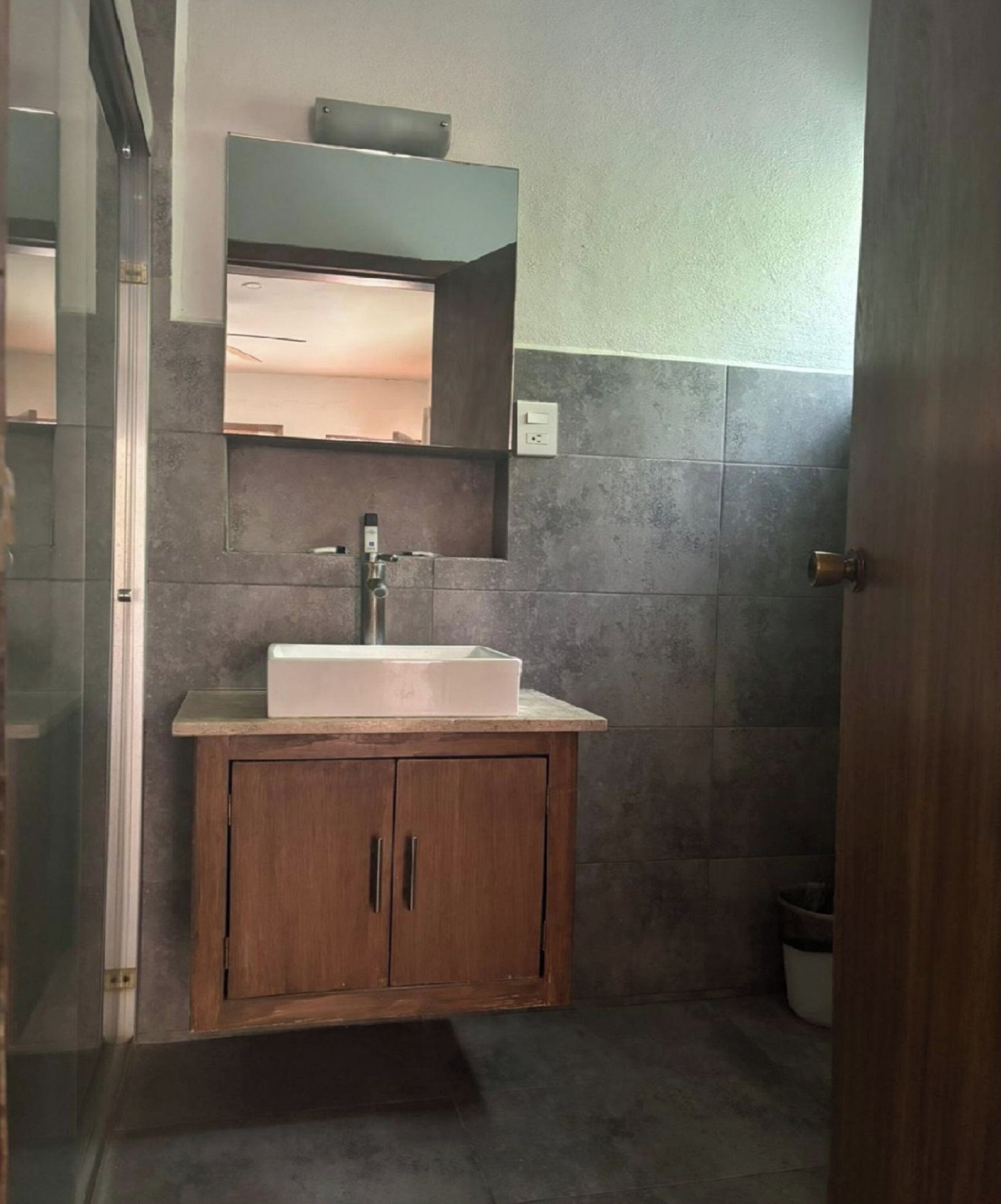 A bathroom with a wooden cabinet, a white sink, and a mirror above it.