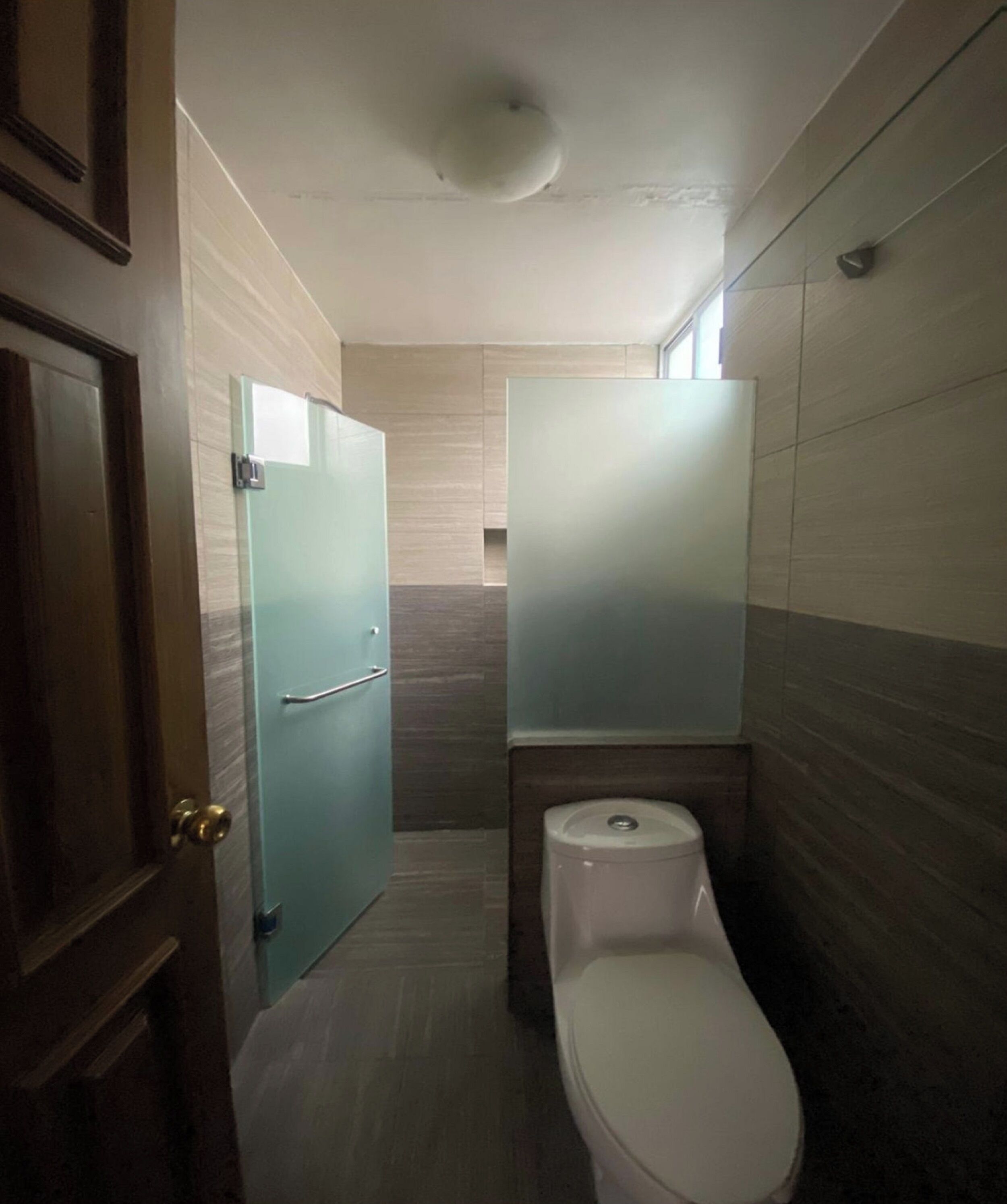 Un bagno stretto con il water, una porta in vetro e una porta in legno.