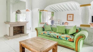 Una sala de estar con chimenea, un sofá verde con cojines estampados y una mesa de centro de madera.