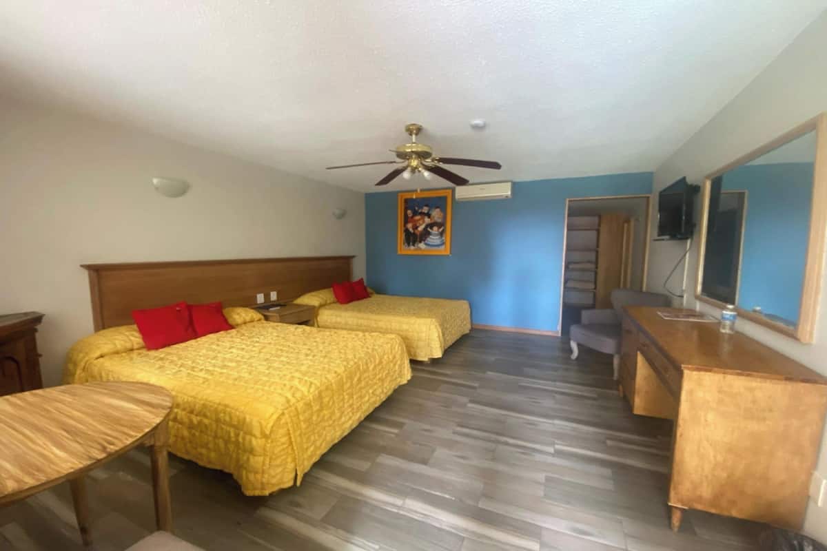 A hotel room with two beds, a wooden desk, a ceiling fan, and a large mirror.