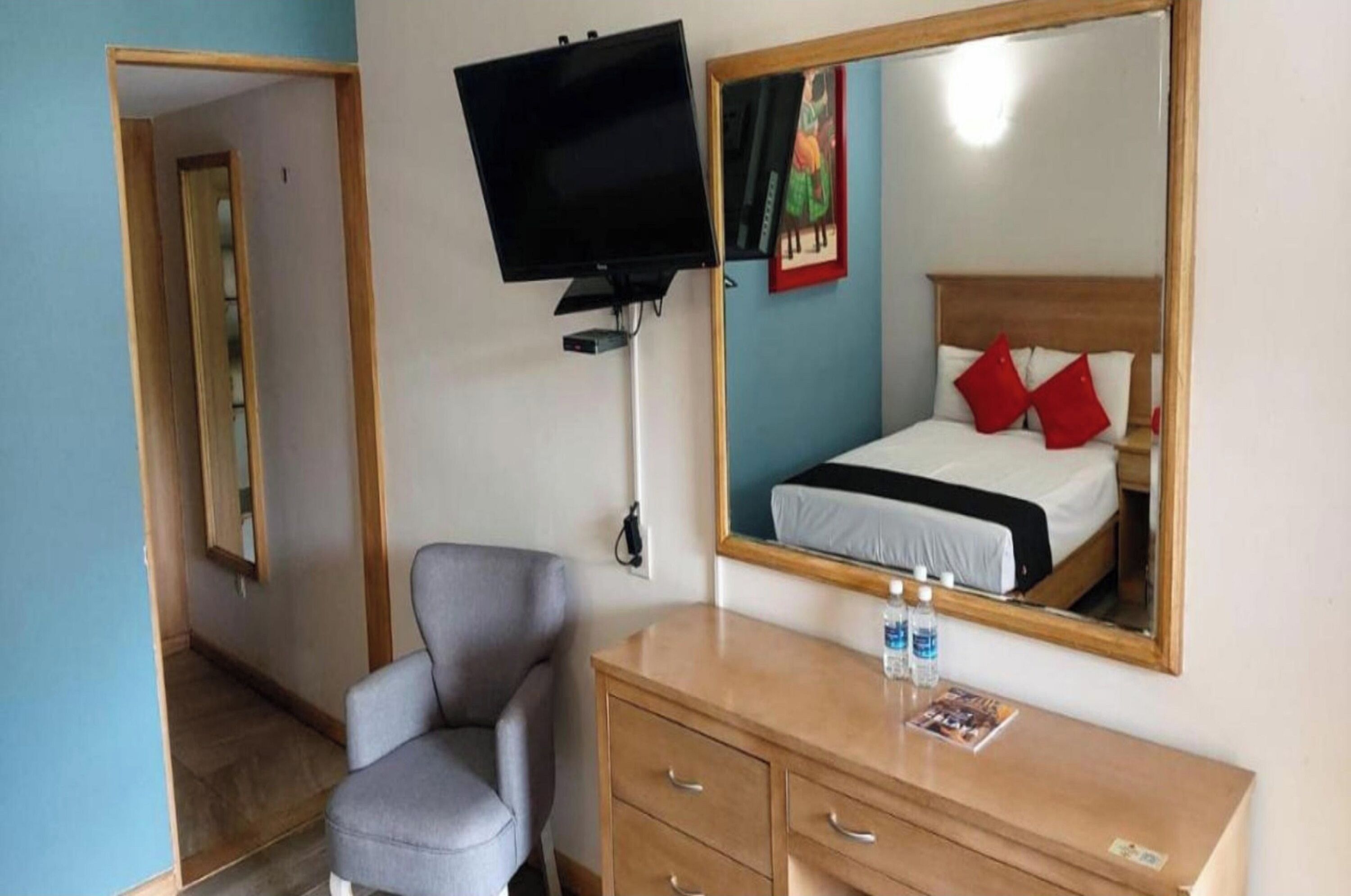 Habitació d'hotel amb un llit, un televisor penjat a la paret, una cadira, un taulell de fusta i un mirall.