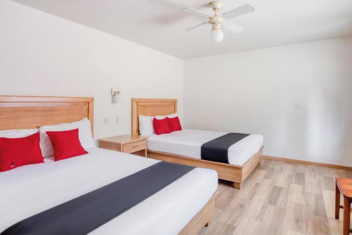 A hotel room with two single beds, wooden headboards, white walls, a ceiling fan, and a wooden floor.