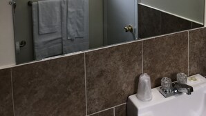 Un baño con un espejo grande, ventana, toallero y lavabo con grifo.