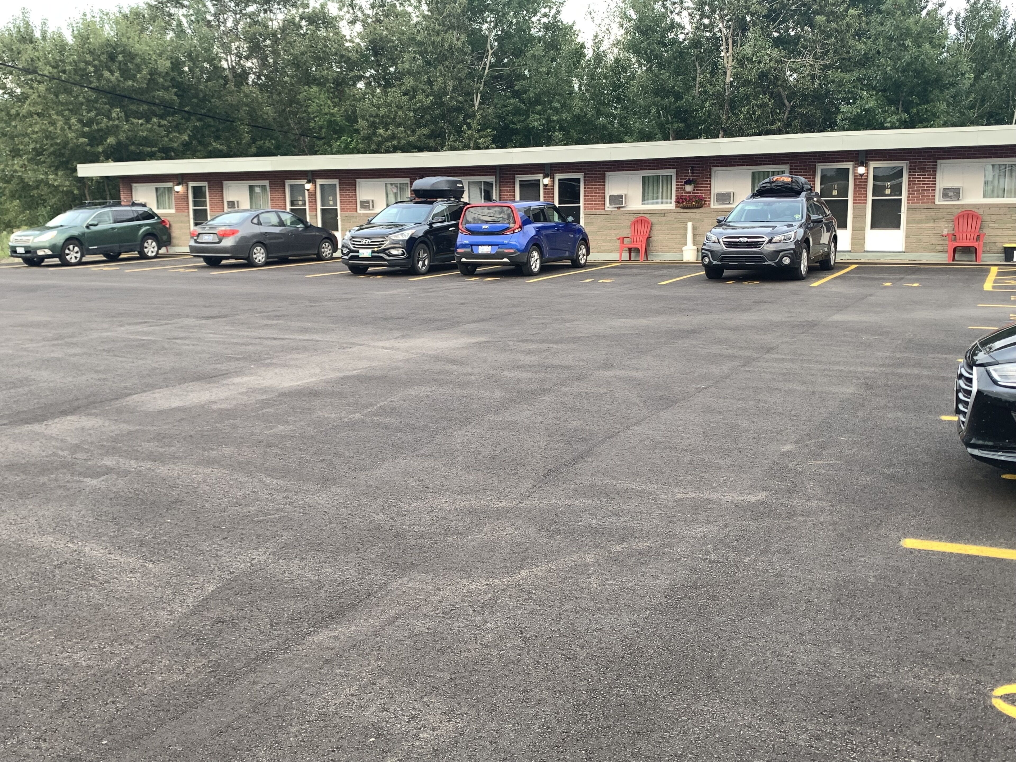 A parking lot with several cars parked in front of a building with numbered doors.