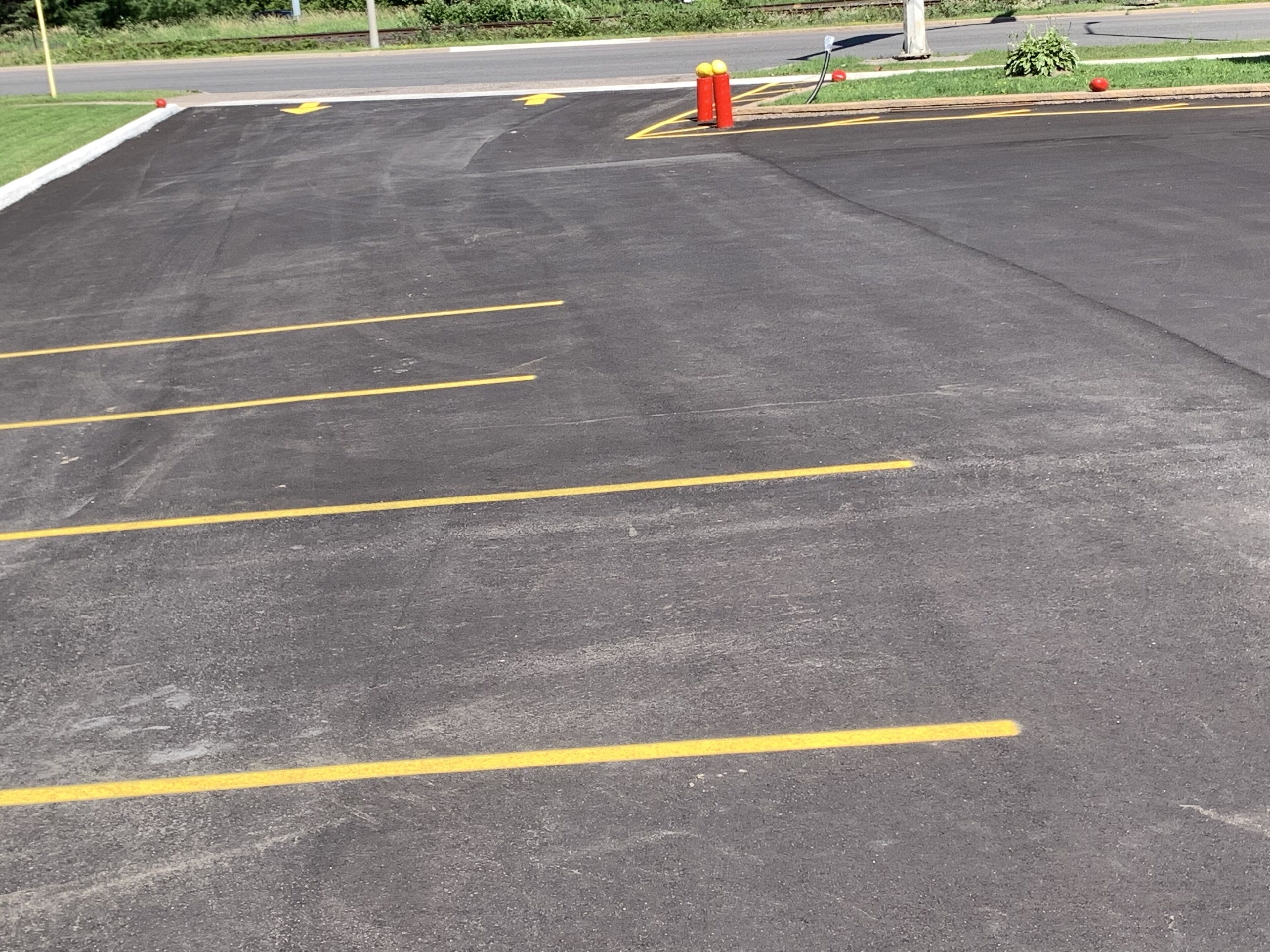 Un parking avec des lignes jaunes délimitant les places et un poteau rouge près du bord du trottoir.