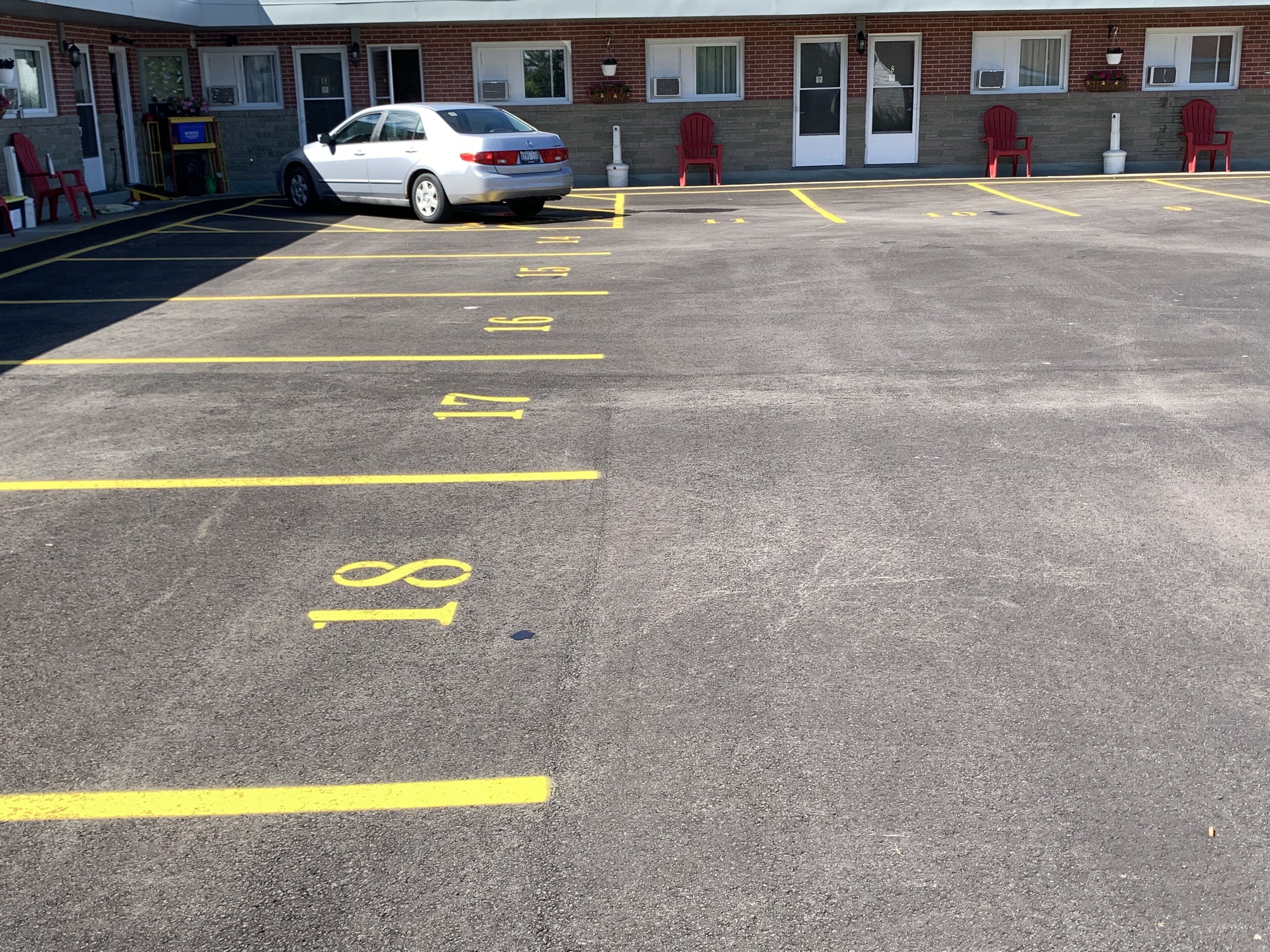 A parking lot with numbered spaces, a white car parked, and a building with red chairs outside.