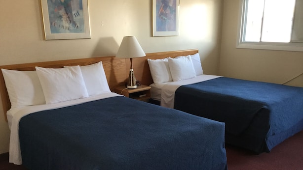 Habitación de hotel con dos camas, cada una con almohadas blancas y colchas azules. Hay una mesita de noche con una lámpara y un cuadro en la pared.