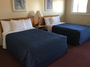 Habitación de hotel con dos camas, cada una con almohadas blancas y colchas azules. Hay una mesita de noche con una lámpara y un cuadro en la pared.