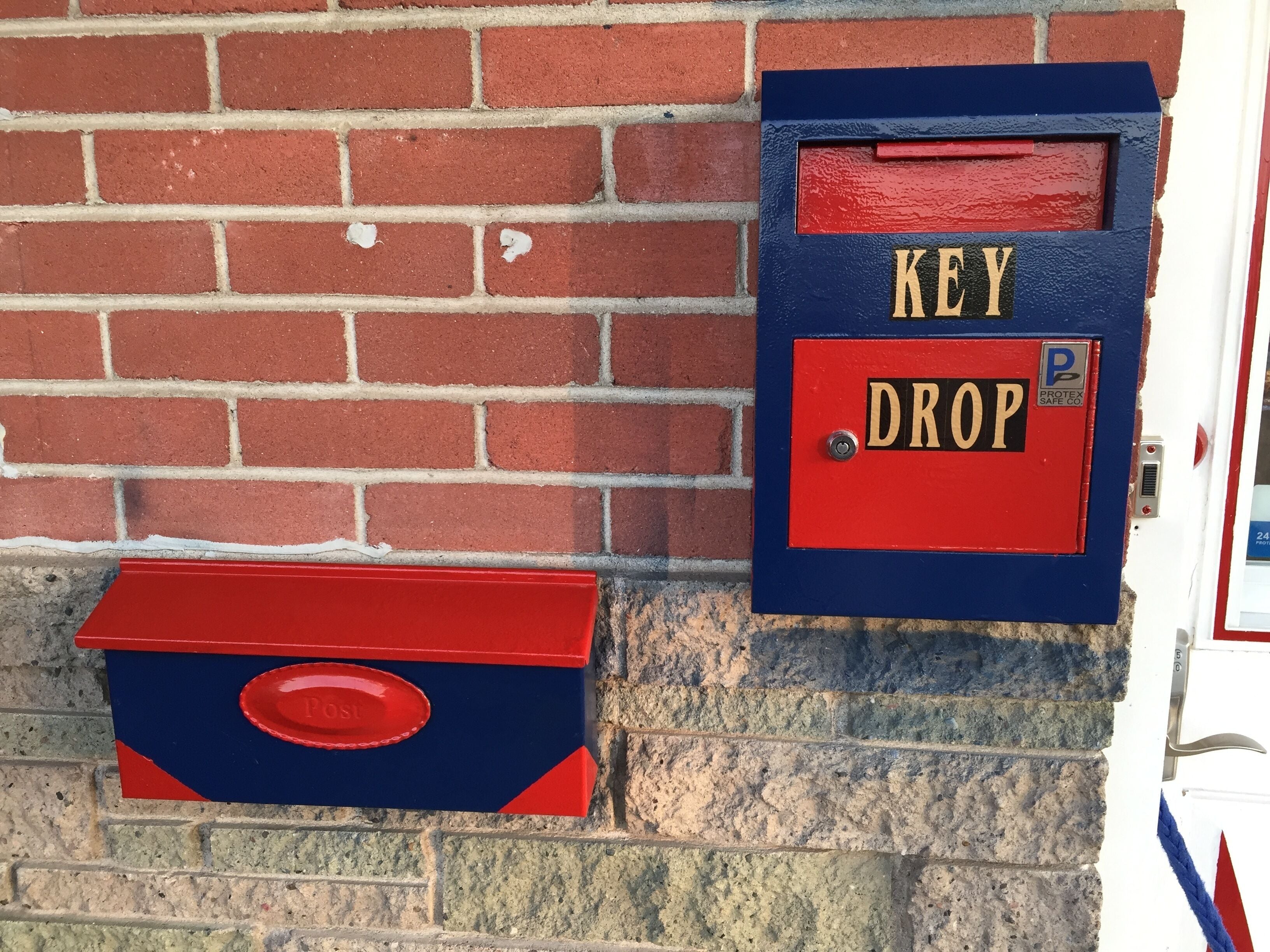 A red and blue key drop box mounted on a brick wall.