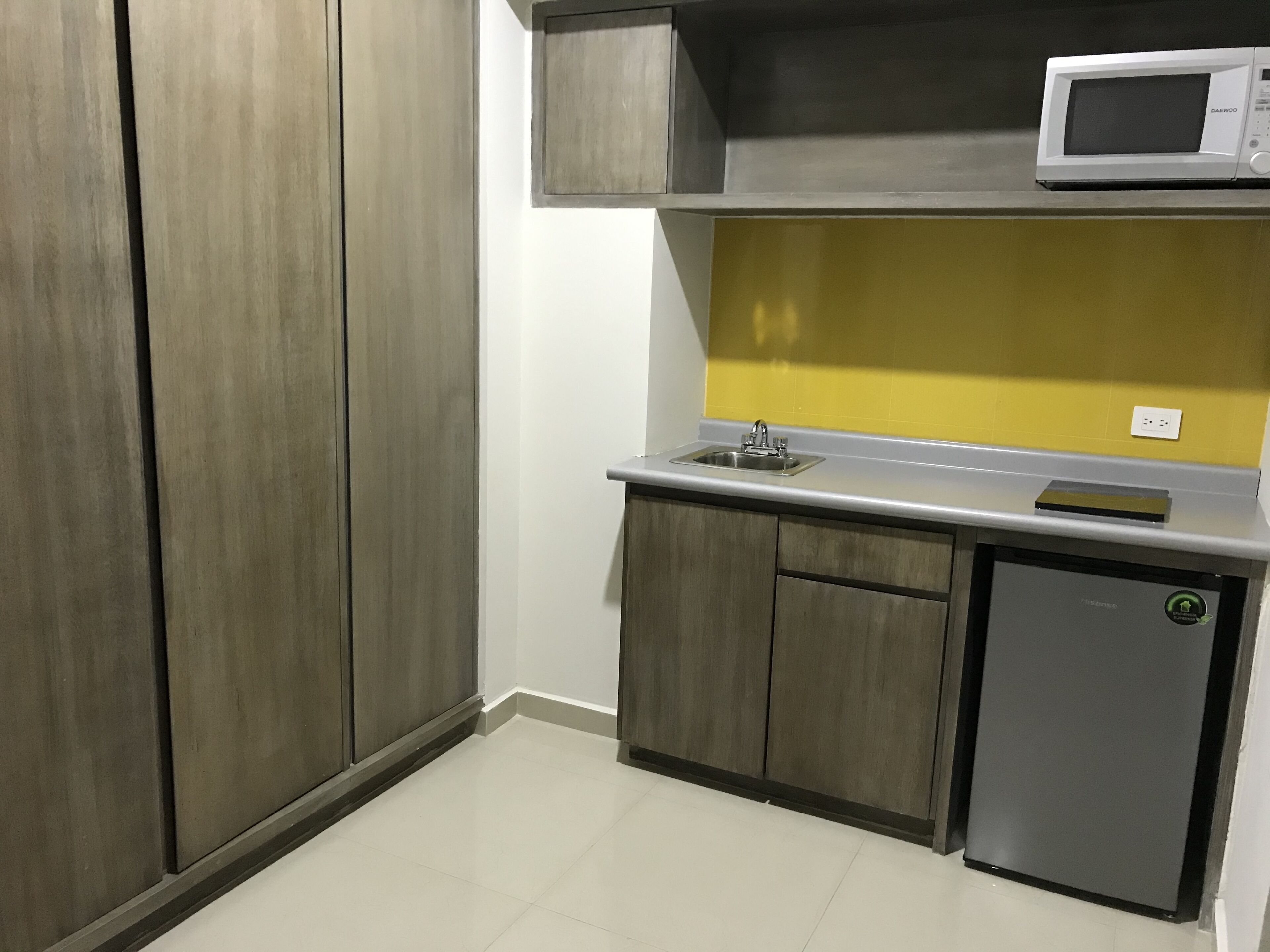 Cocina compacta con microondas, fregadero y nevera pequeña.