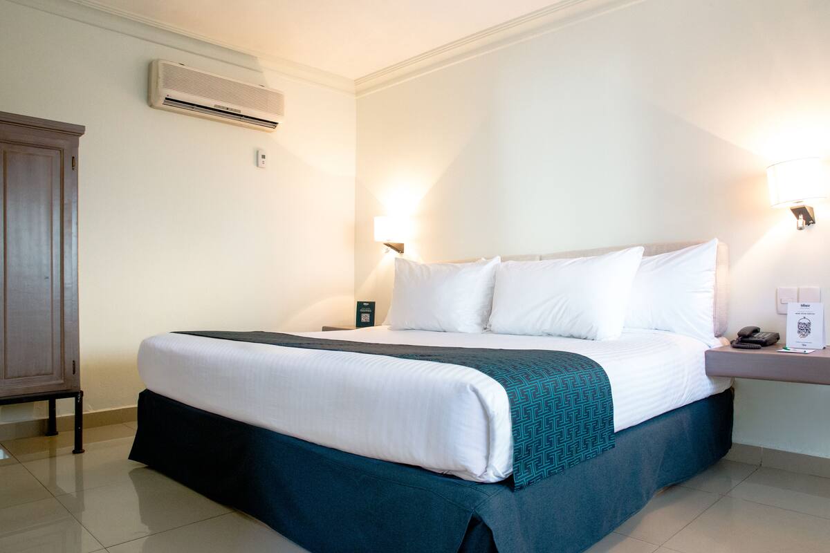 Habitación de hotel con una cama grande, una mesita de noche con lámpara, un aire acondicionado en la pared y un armario de madera.