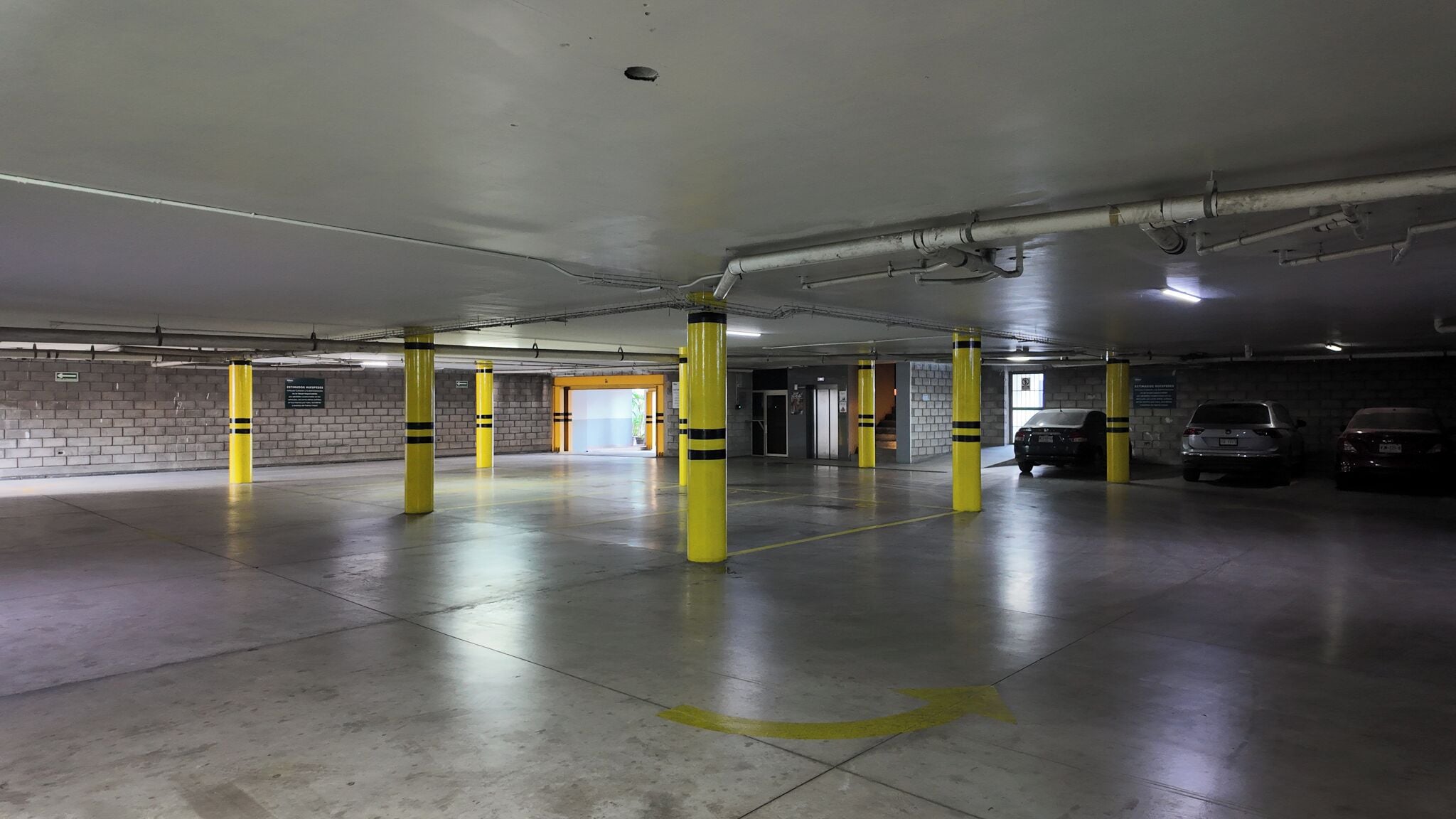 Un estacionamiento de varios niveles con bollards amarillos, pisos de concreto y algunos coches estacionados.
